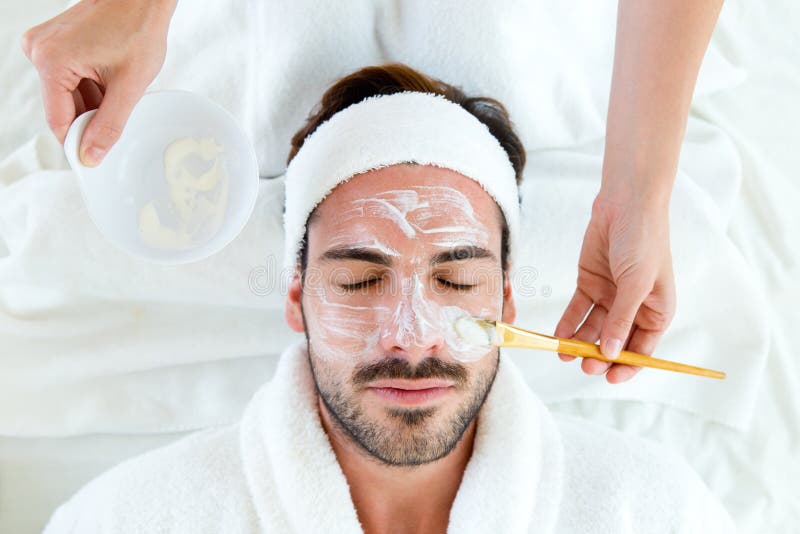 Mens met klei gezichtsmasker in beauty spa