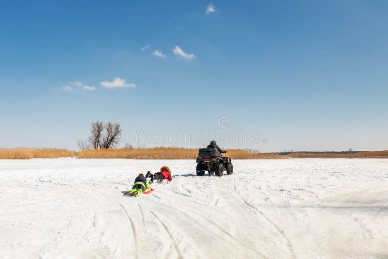 Mens op de berijdende sleeën van ATV quadbike met jonge geitjes in slepen op bevroren meeroppervlakte bij de winter De winter ext stock foto Mens op de berijdende sleeën van ATV quadbike met jonge geitjes in slepen op bevroren meeroppervlakte bij de winter De winter ext stock foto