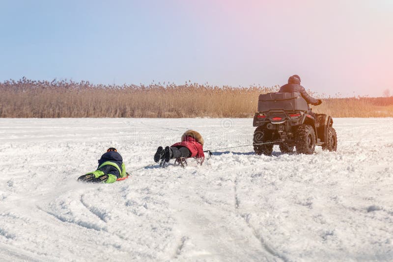 Mens op de berijdende sleeën van ATV quadbike met jonge geitjes in slepen op bevroren meeroppervlakte bij de winter De winter ext royalty-vrije stock foto Mens op de berijdende sleeën van ATV quadbike met jonge geitjes in slepen op bevroren meeroppervlakte bij de winter De winter ext royalty-vrije stock foto