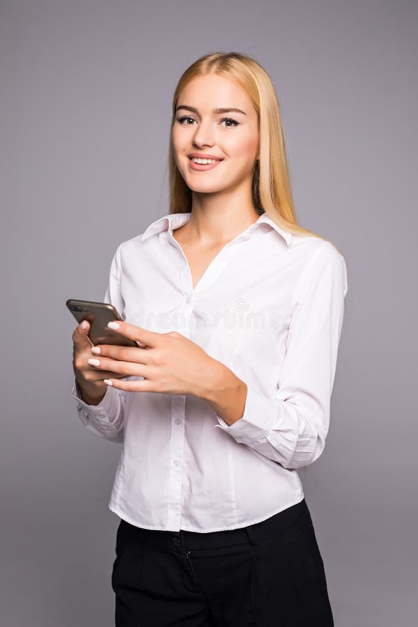 Mensagem de datilografia da jovem mulher no smartphone menina de sorriso bonita que usa seu telefone celular, fundo cinzento do e foto de stock Mensagem de datilografia da jovem mulher no smartphone menina de sorriso bonita que usa seu telefone celular, fundo cinzento do e foto de stock