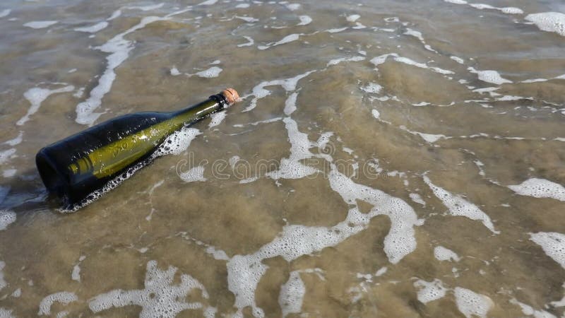 Mensaje secreto dentro de la botella en la orilla con las olas del mar