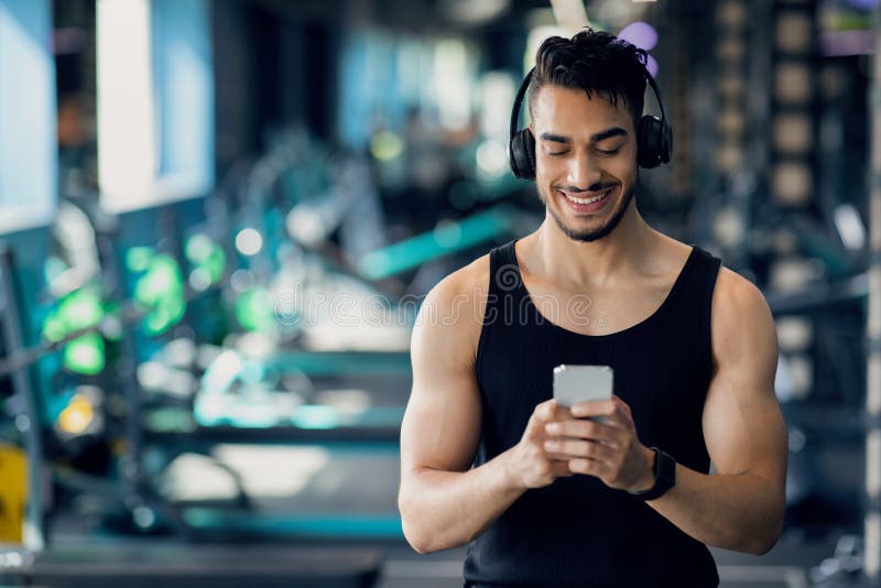 Hombre musculoso atlético en auriculares inalámbricos escuchando música  durante el entrenamiento en el gimnasio
