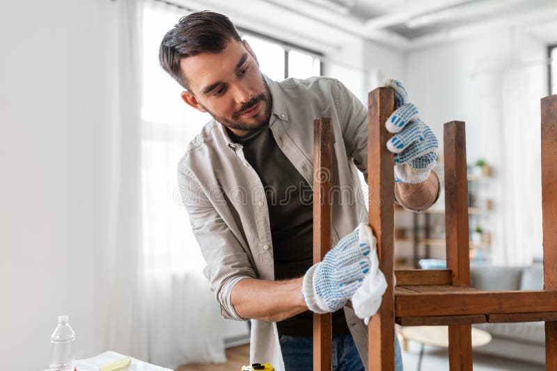 renovation, diy and home improvement concept - man degreasing old wooden table or chair surface with tissue. renovation, diy and home improvement concept - man degreasing old wooden table or chair surface with tissue