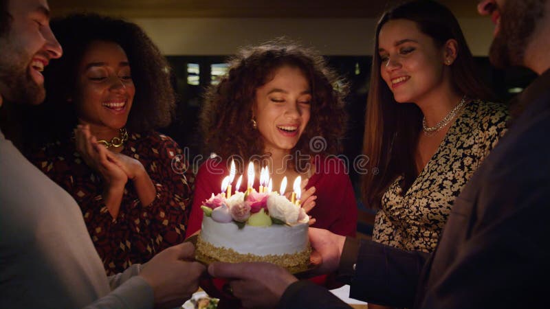 Menschen singen glücklichen Geburtstag zu aufgeregter Frau. Freunde stellen Kuchen auf Party vor.