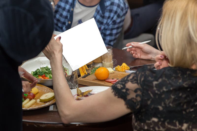 mensen die diner hebben samen terwijl het zitten bij de houten lijst Vrouwelijke hand die Witboek houden royalty-vrije stock afbeelding mensen die diner hebben samen terwijl het zitten bij de houten lijst Vrouwelijke hand die Witboek houden royalty-vrije stock afbeelding