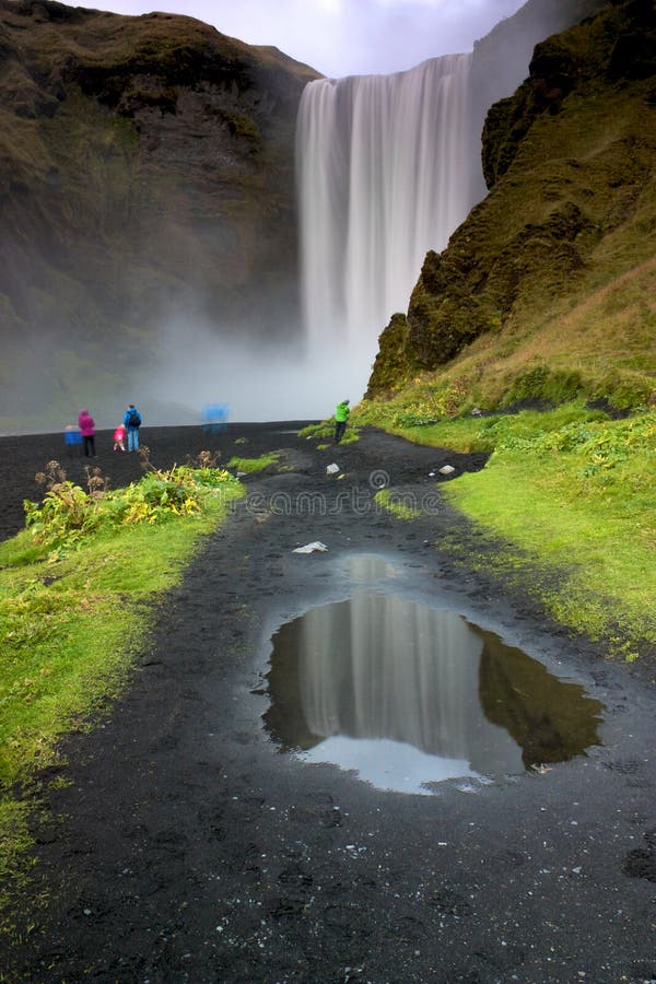 Mensen die in kleurrijke jasjes Waterval Skógafoss bekijken stock fotografie Mensen die in kleurrijke jasjes Waterval Skógafoss bekijken stock fotografie