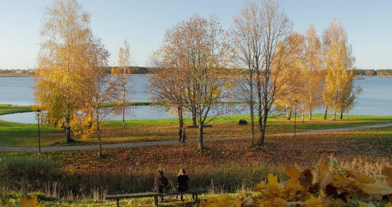 Mensen die met het genieten van van rustig parkgebladerte door meer tijdens de herfst lopen