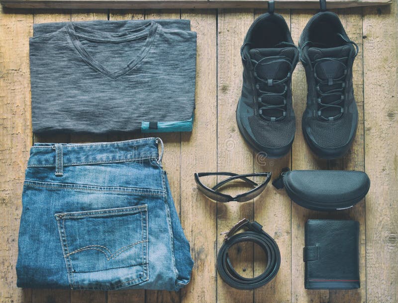 Mensen toevallige uitrustingen Mensenschoenen, kleding en toebehoren op houten achtergrond - grijze t-shirt, jeans, tennisschoene stock fotografie Mensen toevallige uitrustingen Mensenschoenen, kleding en toebehoren op houten achtergrond - grijze t-shirt, jeans, tennisschoene stock fotografie