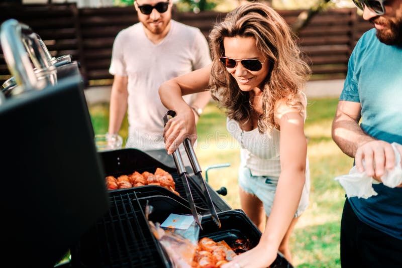 Mensenconcept - Vrienden die een barbecuepartij in aard hebben terwijl het hebben van een het goede tijd, drinken, koken en eten royalty-vrije stock afbeelding Mensenconcept - Vrienden die een barbecuepartij in aard hebben terwijl het hebben van een het goede tijd, drinken, koken en eten royalty-vrije stock afbeelding