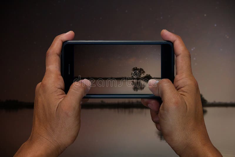 Mensenhand die en mobiel, celtelefoon, slimme telefoonfotografie en Meer in de nacht met de sterren in de hemel houden gebruiken stock fotografie Mensenhand die en mobiel, celtelefoon, slimme telefoonfotografie en Meer in de nacht met de sterren in de hemel houden gebruiken stock fotografie