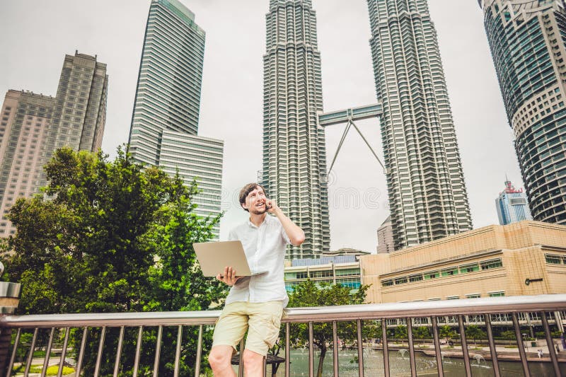 Mensenzakenman of student in toevallige kleding die laptop in een tropisch park op de achtergrond van wolkenkrabbers met behulp v stock foto's Mensenzakenman of student in toevallige kleding die laptop in een tropisch park op de achtergrond van wolkenkrabbers met behulp v stock foto's
