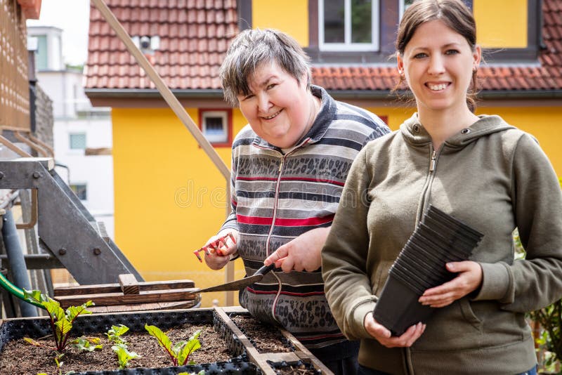 Mentally handicapped woman and her caregiver stand in front of a raised bed in the garden