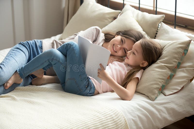Menzogne di riposo adorabile della madre e del derivato sul libro di lettura del letto immagine stock libera da diritti Menzogne di riposo adorabile della madre e del derivato sul libro di lettura del letto immagine stock libera da diritti