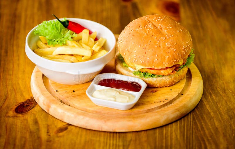 Menú de la hamburguesa Alto bocado de la caloría Hamburguesa y patatas fritas y salsa de tomate en el tablero de madera Concepto foto de archivo libre de regalías Menú de la hamburguesa Alto bocado de la caloría Hamburguesa y patatas fritas y salsa de tomate en el tablero de madera Concepto foto de archivo libre de regalías