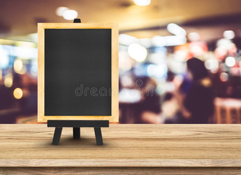 Menú de la pizarra con el caballete en la tabla de madera con el restaurante de la falta de definición imagen de archivo libre de regalías Menú de la pizarra con el caballete en la tabla de madera con el restaurante de la falta de definición imagen de archivo libre de regalías