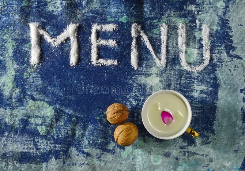 Menú de texto hecho de sal con taza de leche, nueces aisladas en fondo azul escarpado. Menú de texto hecho de sal con una taza de leche, nueces aisladas en un fondo escarpado de color gris azul