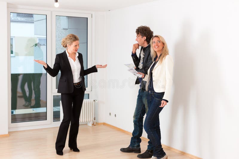 Pares novos que procuram bens imobiliários com corretor de imóveis fêmea foto de stock Pares novos que procuram bens imobiliários com corretor de imóveis fêmea foto de stock