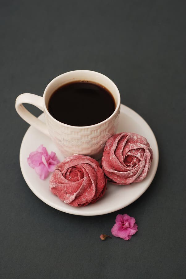 Merengues y taza de café rosados dulces en fondo del gris azul con las flores rosadas Fondo de la primavera con el espacio de la fotografía de archivo Merengues y taza de café rosados dulces en fondo del gris azul con las flores rosadas Fondo de la primavera con el espacio de la fotografía de archivo