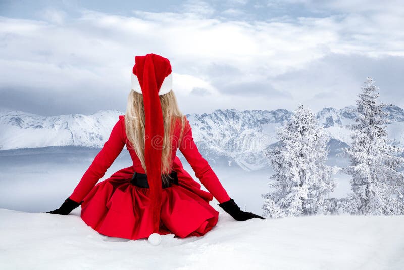 Merry Christmas. Beautiful sexy blonde woman in red dress and Santa clause hat on a background of mountains and snow. Beautiful