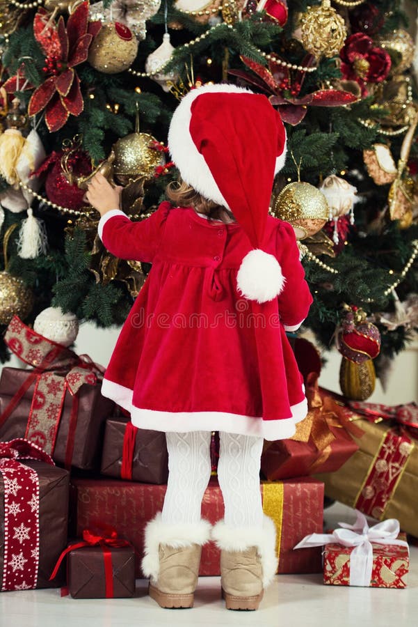 Merry Christmas and Happy Holidays. Cute little child girl is decorating the Christmas tree indoors. royalty free stock photography Merry Christmas and Happy Holidays. Cute little child girl is decorating the Christmas tree indoors. royalty free stock photography
