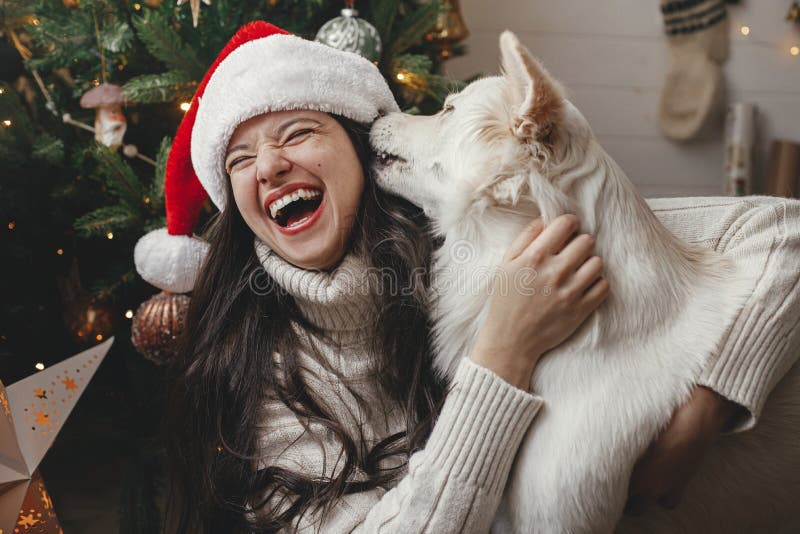 Merry Christmas! Happy woman in santa hat hugging cute dog at stylish christmas tree. Pet and winter holidays. Adorable funny