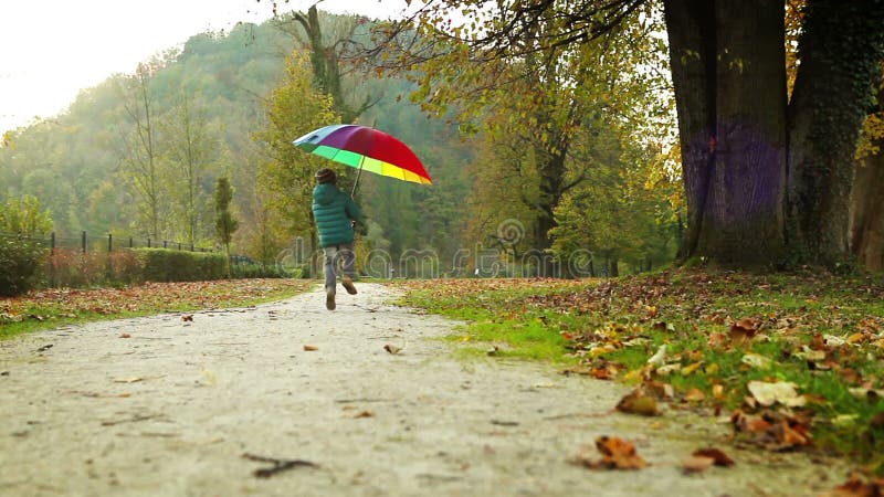Merry little boy jumps with pied umbrella in autumn park