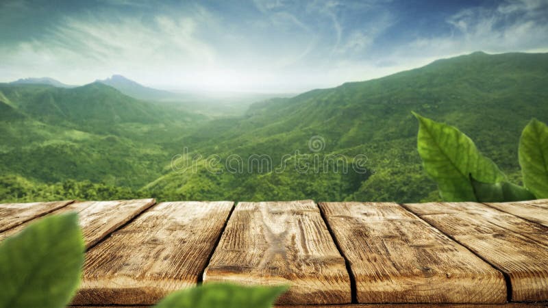 Mesa de madera con fondo de montaña verde. cielo azul con luz solar y hojas pequeñas verdes. fotos de archivo
