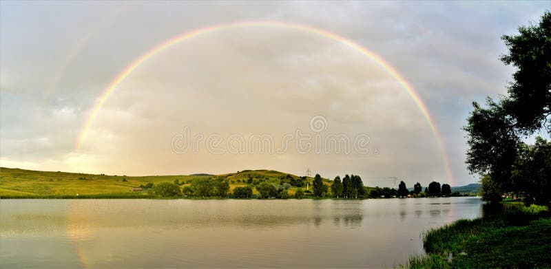 Mesmerizing снимок идеальной rainbow над озером и природными пейзажами стоковые изображения