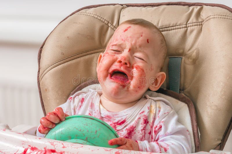 Messy and dirty baby is eating snack and crying