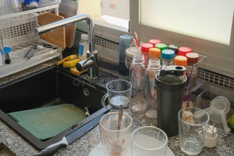 Messy kitchen sink with unwashed plates, cutlery and dirty cutting board on cluttered worktop royalty free stock photo