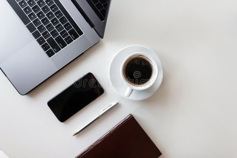 Metaallaptop, een smartphone, een blocnote, een pen en een kop van zwarte koffie op een witte houten lijst Hoogste mening van de stock afbeeldingen Metaallaptop, een smartphone, een blocnote, een pen en een kop van zwarte koffie op een witte houten lijst Hoogste mening van de stock afbeeldingen