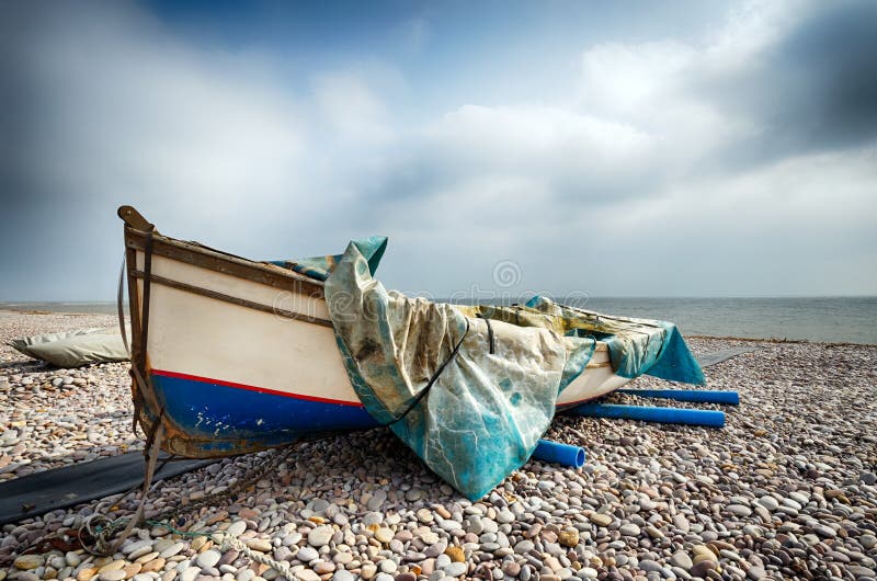 Fishing boat half draped with tarpaulin on the beach at Budleigh Salterton in Devon. Fishing boat half draped with tarpaulin on the beach at Budleigh Salterton in Devon