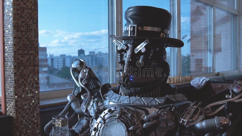 Metal android sitting at table in restaurant with glass of wine on background of view of high-rise buildings of city