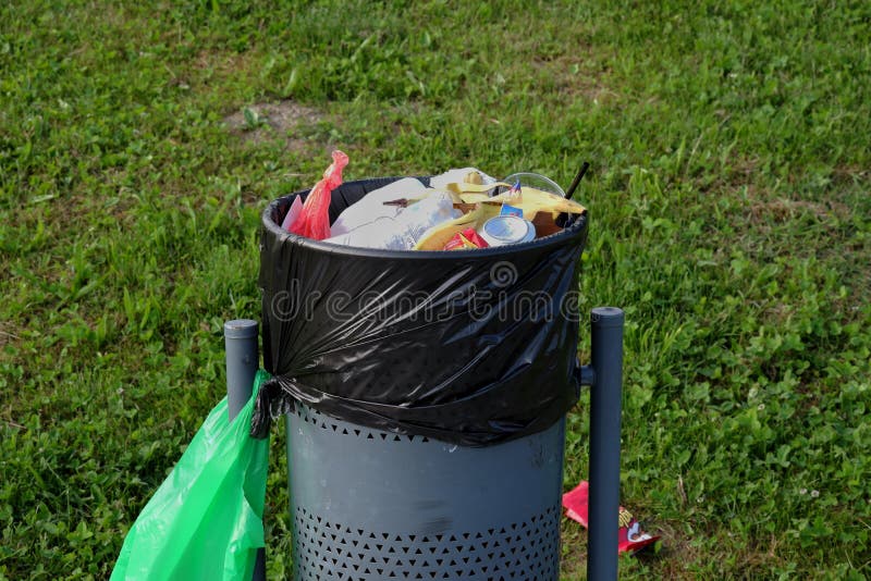 A Metal Bin Full of Rubbish, with a Green Plastic Bag in a Meadow Stock