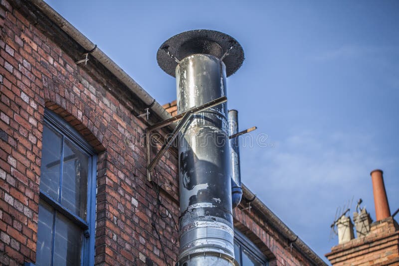 Metal chimney on the old brick house. Ventilation tube chimney on the red brick house. Blue sky in the background.