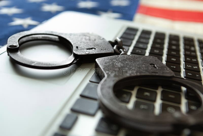 Metal handcuffs over a laptop with an old USA flag on background - close up studio shot royalty free stock image Metal handcuffs over a laptop with an old USA flag on background - close up studio shot royalty free stock image