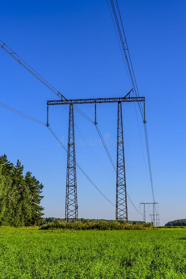 Metal i supporti ed i cavi di una linea di trasmissione ad alta tensione sopra un campo verde nella mattina dell'inizio dell'esta immagini stock libere da diritti Metal i supporti ed i cavi di una linea di trasmissione ad alta tensione sopra un campo verde nella mattina dell'inizio dell'esta immagini stock libere da diritti