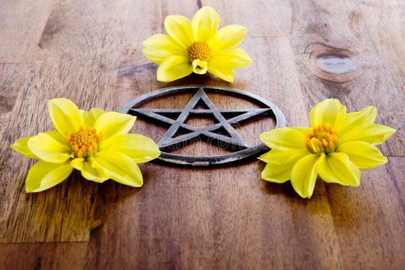 Metal pentagram with three yellow dahlia flowers on wooden background