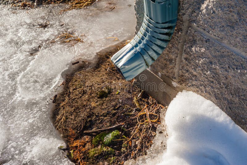 Metal pipe dripping water on melting snow.