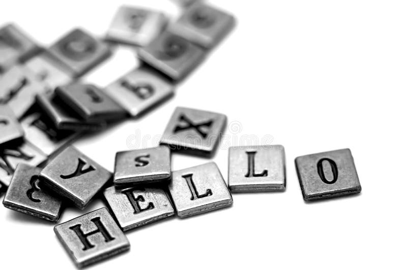 Metal scrapbooking letters spelling Hello. They lay on a white background and there is a bunch of other letters laying by.