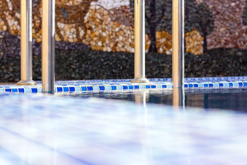 A metal swimming pool safe ladder (skimmer) on the entrance to the home inground poolside with the blue clean water stock photo A metal swimming pool safe ladder (skimmer) on the entrance to the home inground poolside with the blue clean water stock photo