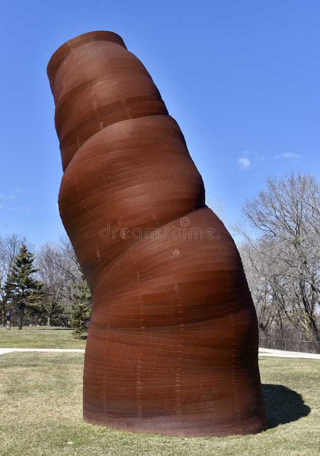 This is an early Spring picture of a piece of public art titled: Metalmatic, on display at the Skokie Northshore Sculpture Park located in Skokie, Illinois in Cook County. This piece was created by Kari Reardon. This large, organic form was made from a huge industrial coil of steel. The coil was suspended downward and, as it moved and dropped, it was adjusted to the position desired and then welded together. The goal was to take a hard manmade material and transform it into a soft billowing form that has a feeling of growth and movement. This picture was taken on April 7, 2018.