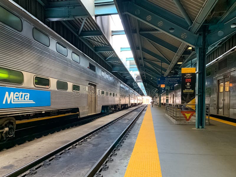 Metra trains on tracks  in terminal at Ogilvie Transportation Center as passenger waits on platform at track 3 for train to arrive