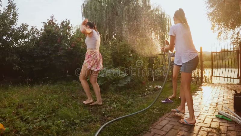 Metragem do movimento lento da família alegre feliz que espirra a água da tubulação de mangueira no jardim