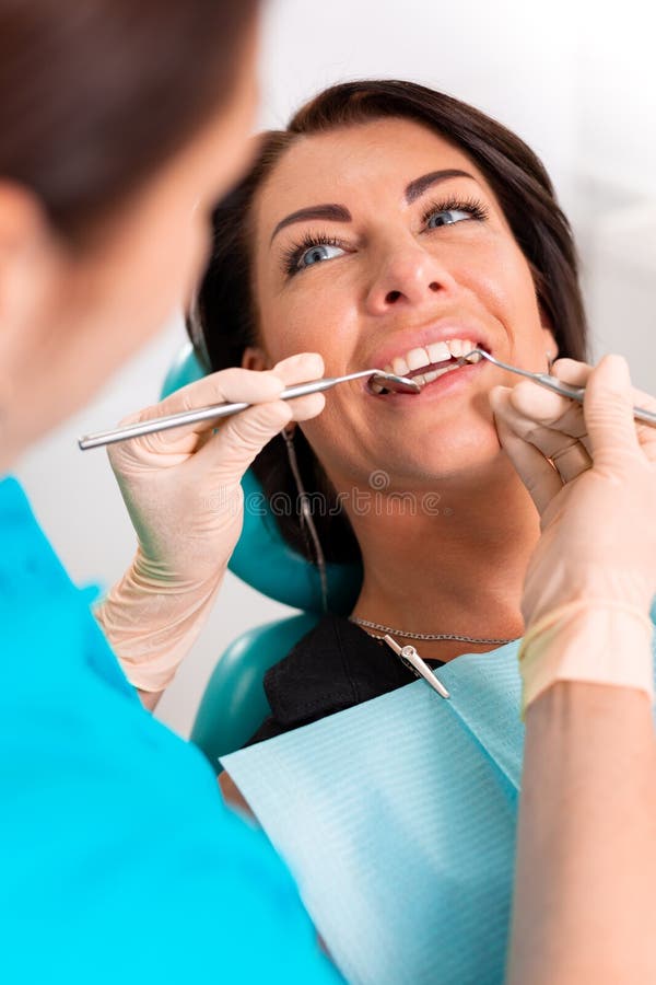 Mettendo i ganci dentari ai denti del ` s della donna all'ufficio dentario Dentista esaminare paziente femminile con i ganci in d fotografia stock Mettendo i ganci dentari ai denti del ` s della donna all'ufficio dentario Dentista esaminare paziente femminile con i ganci in d fotografia stock