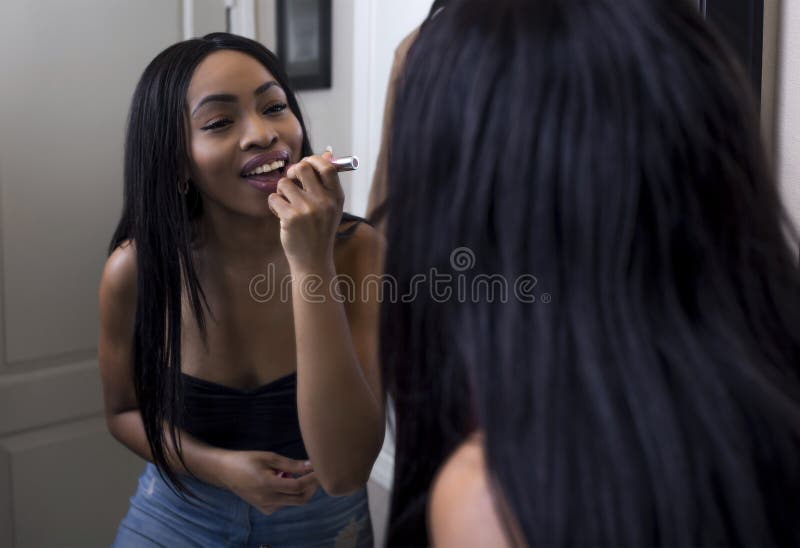 Mettere femminile nero sul rossetto in un bagno domestico. Prepararsi femminile nero per una data e mettere sul rossetto davanti ad uno specchio del bagno Sopra la spalla il colpo cinematografico descrive la donna che applica la lucentezza del labbro o del rossetto