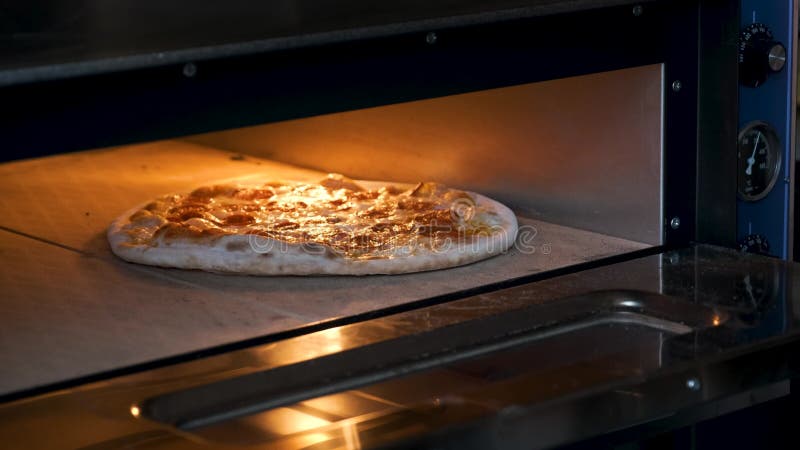 Mettere la pizza con salame piccante nel forno in una cucina ristorante.