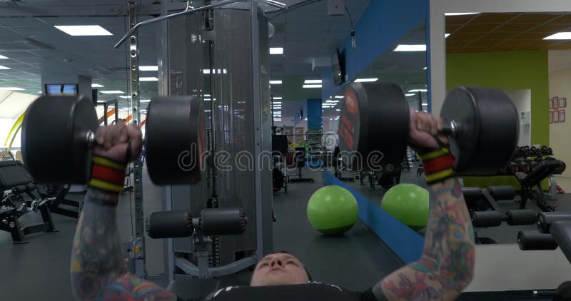 Metà di uomo di età che fa esercizio pesante con le teste di legno in palestra Allenamento della stampa di banco della palestra G