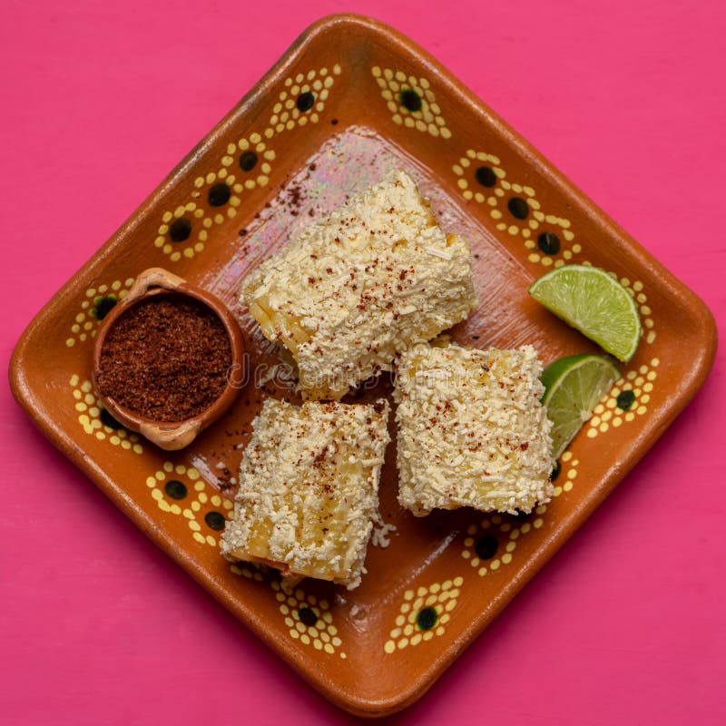 Mexican corn on the cob also called elotes with cheese and mayonnaise on pink background