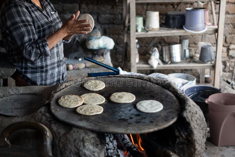 Woman makes corn tortillas by hand and cooks them on a large clay